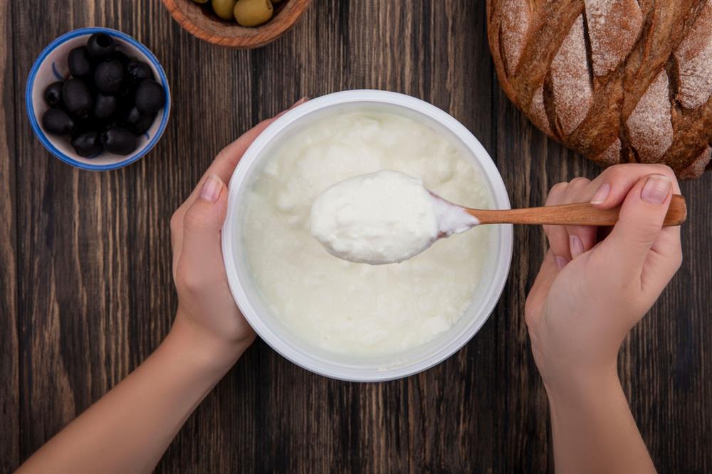  A bowl of yogurt and a woman's hand taking a spoonful of yogurt.